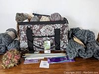 Knitting bag filled with yarn balls, knitting needles in front, and partially knitted chunky blanket on the right