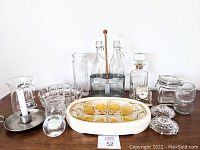 Photo of the entire lot showing all the items including the clock, serving dishes, water bottles in carrier, decanter, candle holders, and other glass and ceramic items.