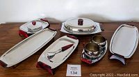 Photo showing large covered oval chrome serving dish, two rectangular trays, three smaller trays, and condiment cups with cherry Bakelite handles.