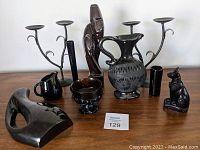 Photo showing collection of black ceramic art pieces including vase, pitchers, bowl, abstract sculpture, Egyptian cat figurine, and wrought iron candle holders