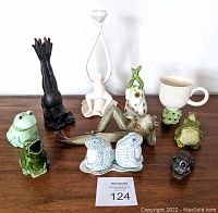 Top-view showing whole lot of 11 collectible ceramic frog figurines in various styles and colors arranged on a wooden surface.