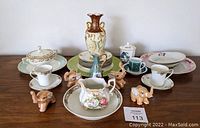 Full lot view showing all porcelain china pieces, cups, saucers, plates, creamer, a tall vase, and six brown lusterware elephant figurines arranged on a wooden table.