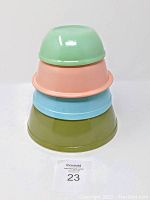 Four vintage Pyrex mixing bowls stacked nested together showing avocado green, peach, light blue, and light green colors.