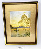 Frontal image of the framed E. Stephens Dufex iridescent aluminum foil print showing the fisherman on a lake and gold-toned trees with flying birds.