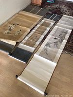 Three Asian scrolls laid flat, showing full length and fabric borders on wooden rods.