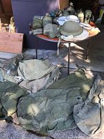 Photo showing the lot with canvass duffel bags, canteen belts, mess kits, helmet and other gear on and around a table