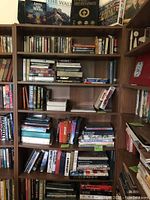 Six-shelf wooden bookcase filled with assorted books and top shelf puzzle boxes