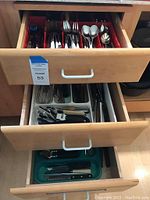 Three open drawers with red, white and green utensil organizer trays holding flatware and utensils