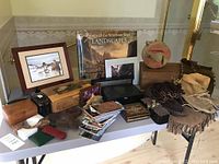 Table view of assorted American West décor items including framed prints, book, boxes and leather goods
