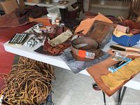 Wide view showing various leather pieces, tools, and copper sheets on table including brushes, twine, and punch.