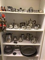 Full shelving unit showing various vintage pewter items such as small pitchers, bowls, teapots, and figures neatly arranged.