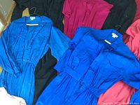 Two electric blue jumpsuits with short sleeves and button fronts against pink and black garments