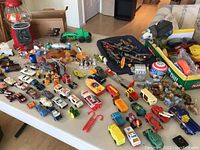 Wide view of various small vintage toys displayed on table, including model cars, figurines, airplanes, and dispenser.