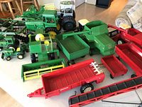 Full overview of the lot items on table showing green tractors, red trailers, and farm equipment