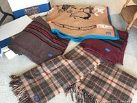 Overview of five folded and spread blankets including two plaid, striped and patterned designs