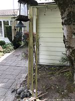 Photo showing the long brass tube wind chime with wooden ends positioned outdoors next to a tree and some stone mulch.