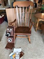 Wooden rocking chair with reproduction wall telephone mounted on the side, includes instruction manuals and packaging materials on the floor.