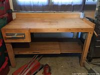 Full view of wooden work bench including vice on the left and bottom shelf. Shows overall bench size and design.