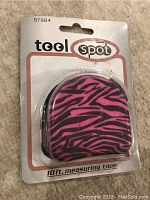 Photo of Tool Spot 10-foot measuring tape in packaging with pink and black zebra print casing.