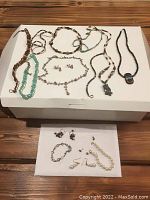 Overall lot of costume jewelry including multiple necklaces and earrings laid out on white and brown backgrounds