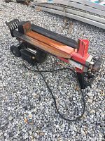 Side angle showing the full length of the electric log splitter with motor, electrical cord, rusted beam, and wedge