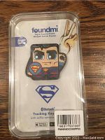 Photo of Superman Foundmi Bluetooth tracking keychain in original packaging showing cartoon Superman face, DC and Bluetooth branding, barcode and app store icons.