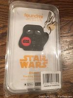 Plastic packaged black Darth Vader Star Wars keychain with red logo on front, sealed in retail packaging with barcode and app download information.
