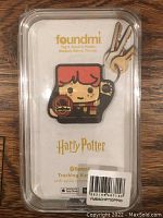 Foundmi Harry Potter style Bluetooth tracking keychain inside its original clear plastic package on a wooden surface.