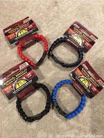 Four survival bracelets in red, dark blue, black, and blue shown together flat on floor with packaging