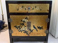 Front view of black lacquer Asian style cabinet with gold floral and bird panels