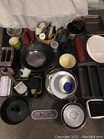 Wide view of assorted kitchenware on floor showing pots, pans, kettle, baking trays, utensil basket, and more.