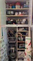 Cabinet filled with various baking supplies such as plastic containers with lids, metal mixing bowls, baking sheets, rolling pin, measuring cups, baking utensils, and storage boxes.