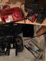 Various tools and hardware on floor including drill bit set in red case, black corded jigsaw, black sander, and small hardware in bags.