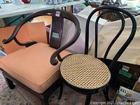Overall view of Chinese horseshoe armchair with peach cushion alongside black bistro chair with cane seat.