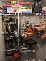 Shelf with various boxed food wraps and freezer bags on top shelf, metal baking pans including copper molds hanging below, electric buffet warmer appliance on lower shelf, and kitchen utensils and appliances on bottom shelf.