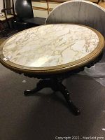 Full view of circular dining table with marble top installed, positioned on dark carpet, with other furniture in background.
