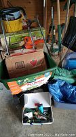 View showing manual lawn spreader, cardboard boxes, plastic bin with small tools and hose spray heads.