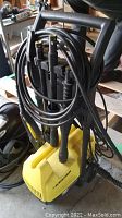 Yellow Karcher power washer with hose and multiple spray nozzles held on the front holder