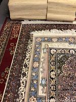 Four stacked area rugs partially covering textured wallpaper rolls