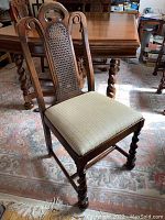 Front view of a wooden dining chair with cane back and beige upholstered seat showing the style and finish.