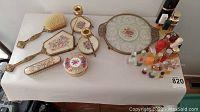 Full overview of vanity items including mirror, brushes, candle holders, decorative box, tray, and perfumes on white table