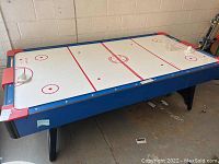 Full view of the air hockey table with blue and red edges and white playing surface marked for hockey.