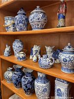 Full view of three shelves showcasing various blue and white pottery pieces including jars, vases, figurines, and covered containers arranged on wooden shelving.
