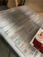 Plastic tote filled with assorted music CDs inside jewel cases, covered with a translucent lid.