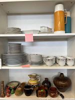 Shelves with stacked plates, cups, and decorative pottery items.