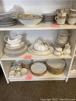 Full view of three shelves with assorted china plates, bowls, teacups, saucers, sugar bowl, and creamer.
