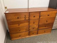 Front angle view showing the dresser with 12 drawers, visible scratches and scuff marks on wood surface.