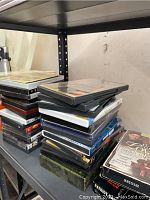 Stack of assorted DVDs piled on a metal shelf, some titles partially visible.