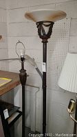 Three different styled dark bronze/copper toned floor lamps. One has a frosted glass torchiere shade, one is missing a shade.