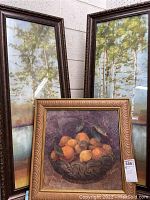 Two tall framed nature prints featuring trees leaning against a wall, with a smaller still life fruit print in front